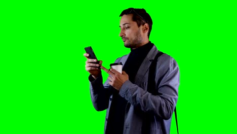 Mann-in-Anzug-und-schwarzen-Sonnenbrillen-Nutzung-mobiler-und-halten-Kaffee-Tasse.-Green-Screen-Aufnahmen.