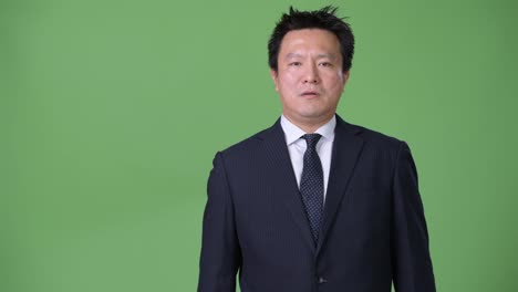 Mature-Japanese-businessman-against-green-background