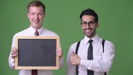 Two-young-multi-ethnic-businessmen-working-together-against-green-background