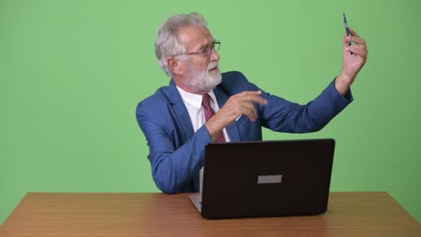 Handsome-senior-bearded-businessman-against-green-background