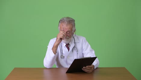 Handsome-senior-bearded-man-doctor-against-green-background