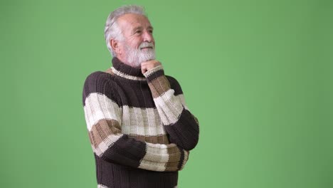 Handsome-senior-bearded-man-wearing-warm-clothing-against-green-background