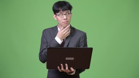 Young-Asian-businessman-thinking-while-using-laptop