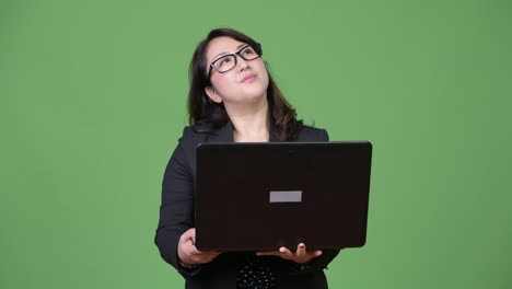 Mature-beautiful-Asian-businesswoman-using-laptop-against-green-background