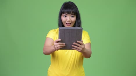 Beautiful-happy-Asian-woman-using-digital-tablet-and-looking-surprised