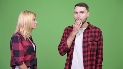 Young-woman-whispering-to-young-man-and-looking-shocked