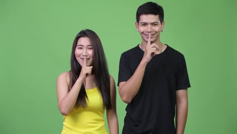 Young-happy-Asian-couple-with-finger-on-lips-together