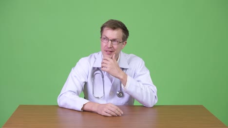 Portrait-Of-Young-Happy-Man-Doctor-Sitting-And-Thinking