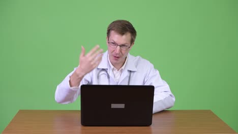 Man-Doctor-Sitting-And-Using-Laptop-Computer-While-Talking-And-Greeting-Patient