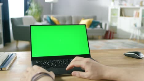 Man-Uses-Laptop-with-Green-Mock-up-Screen-While-Sitting-at-the-Desk-in-His-Cozy-Living-Room.