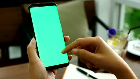 Imágenes-de-4K.-cierre-a-mano-mujer-elegante-piedra-de-afilar-con-pantalla-verde-en-la-cafetería,-deslice-el-dedo-en-la-pantalla-del-teléfono-para-contenido-de-lectura-móvil