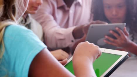 Teacher-sitting-with-school-kids-using-tablets-in-class