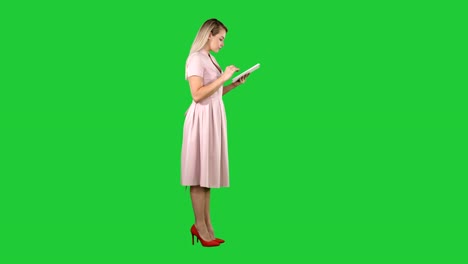 Junge-Frau-in-rosa-Kleid-Seitenansicht-mit-Tablet-auf-einem-Green-Screen,-Chroma-Key