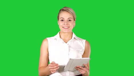 Young-smiling-business-woman-with-tablet-computer-turning-pages-and-looking-in-to-the-camera-on-a-Green-Screen,-Chroma-Key