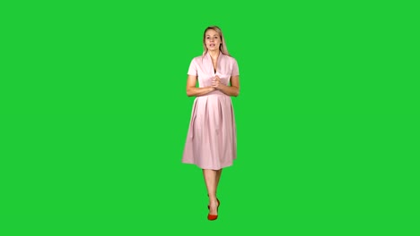 Happy-young-woman-inpink-dress-is-walking-towards-camera-and-talking-on-a-Green-Screen,-Chroma-Key