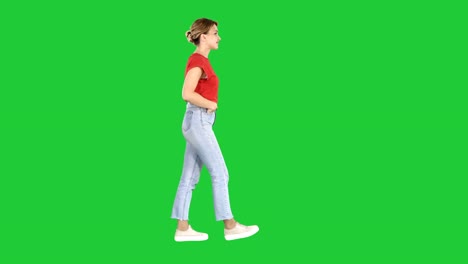 Fit-girl-holding-her-hands-in-the-pockets-of-blue-jeans-walking-on-a-Green-Screen,-Chroma-Key