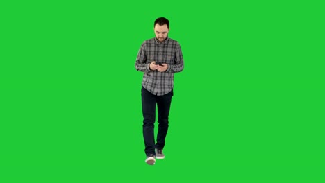 Young-man-walking-and-using-a-phone,-messaging-on-a-Green-Screen,-Chroma-Key