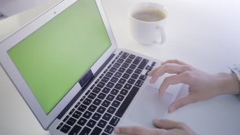 Young-caucasian-woman-in-her-30s-using-her-laptop-with-a-green-screen-to-insert-new-content