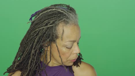 Older-African-American-woman-with-dreadlocks-looks-upset-and-looks-down,-on-a-green-screen-studio-background