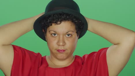 Woman-wearing-a-hat-smiles-and-dances,-on-a-green-screen-studio-background