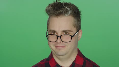 Young-man-with-glasses-staring-ahead,-on-a-green-screen-studio-background