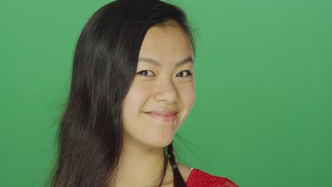 Young-Asian-woman-smiling-and-being-playful,-on-a-green-screen-studio-background