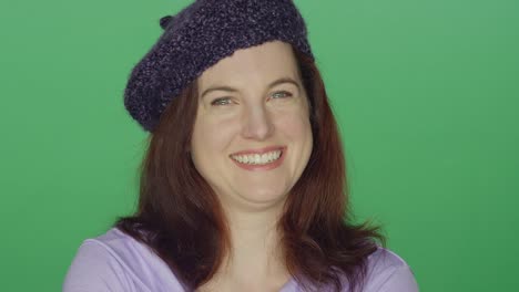 Young-redhead-woman-wearing-a-beret-laughing-and-smiling,-on-a-green-screen-studio-background