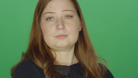 Young-redhead-woman-tries-to-act-serious-but-begins-to-laugh,-on-a-green-screen-studio-background