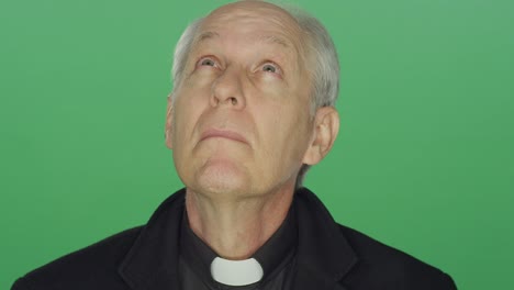 Older-priest-prays-to-the-heavens-and-smiles,-on-a-green-screen-studio-background