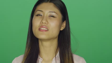 Beautiful-Asian-woman-smiling-and-being-seductive,-on-a-green-screen-studio-background