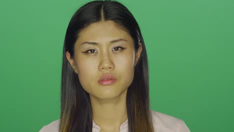 Beautiful-Asian-woman-stares-ahead-and-then-smiles,-on-a-green-screen-studio-background