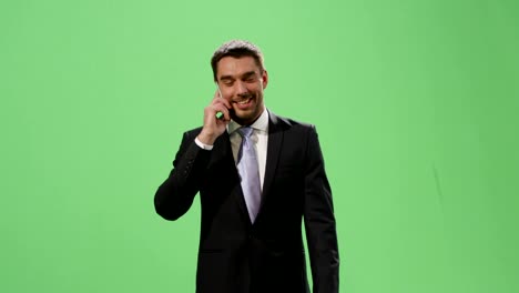 Businessman-in-a-suit-is-walking-and-talking-on-mobile-phone-on-a-mock-up-green-screen-in-the-background.