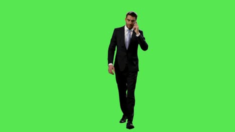 Businessman-in-a-suit-is-walking-and-talking-on-mobile-phone-on-a-mock-up-green-screen-in-the-background.