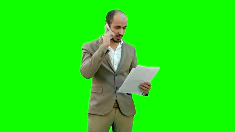 Junger-Mann-im-Anzug-am-Telefon-sprechen-und-halten-Papiere-auf-einem-Green-Screen,-Chroma-Key