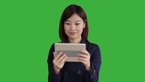 Joven-asiático-llevando-un-abrigo-azul.-Con-el-Smartphone,-tableta-Digital-y-mirando-a-cámara.-Mujer-de-pie-delante-de-una-pantalla-verde-para-Chroma-Key.