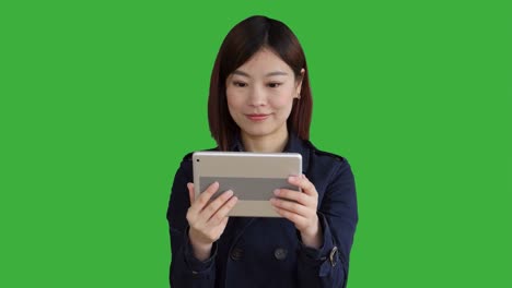 Junge-asiatische-Frau-trägt-einen-blauen-Mantel.-Verwendung-von-Smartphone,-Digital-Tablette-und-Blick-in-die-Kamera.-Frau-stand-vor-einem-Greenscreen-für-Chroma-Key.