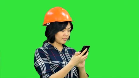 Architektin-mit-orange-Helm-mit-Smartphone-auf-einem-Green-Screen,-Chroma-Key