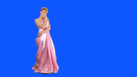 Beautiful-girl-in-pink-satin-bedsheet-poses-for-camera-at-blue-background