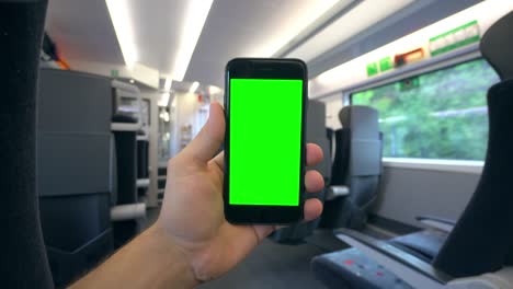 Mano-sosteniendo-un-teléfono-con-una-pantalla-verde-en-el-tren