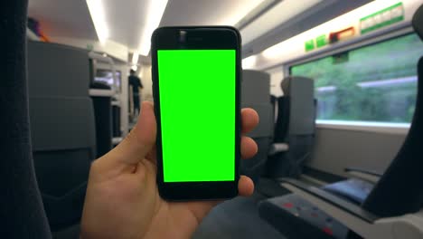 Hand,-die-eine-Handy-mit-einem-Green-Screen-auf-dem-Zug