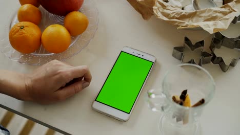 Nahaufnahme-von-Frauenhand-Smartphone-mit-Greenscreen-am-Küchentisch-zu-Hause-Surfen
