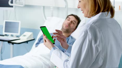 Profesional-del-doctora-habla-con-enfermo-paciente-acostado-en-la-cama,-ella-utiliza-teléfono-móvil-de-pantalla-verde.-Tecnología-médica.