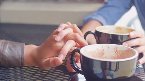 Nahaufnahme-von-ein-paar-Hand-in-Hand-über-den-Tisch-hinweg-an-einem-Kaffee-Datum