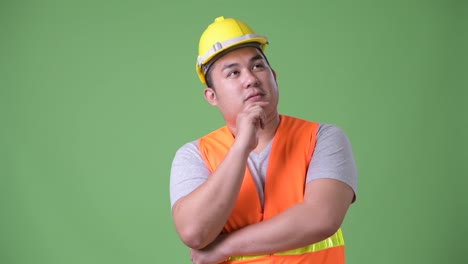 Young-handsome-overweight-Asian-man-construction-worker-against-green-background