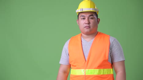 Young-handsome-overweight-Asian-man-construction-worker-against-green-background