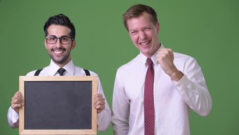 Two-young-multi-ethnic-businessmen-working-together-against-green-background