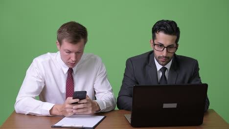 Two-young-multi-ethnic-businessmen-working-together-against-green-background