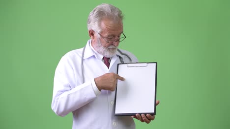 Handsome-senior-bearded-man-doctor-against-green-background