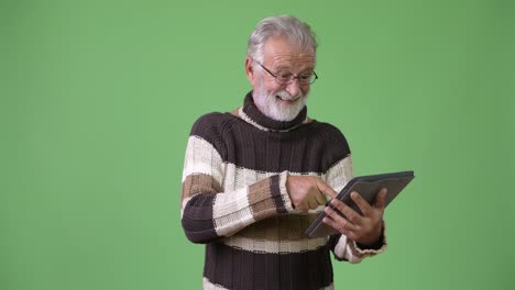 Gut-aussehend-Senior-bärtiger-Mann-in-warme-Kleidung-vor-grünem-Hintergrund