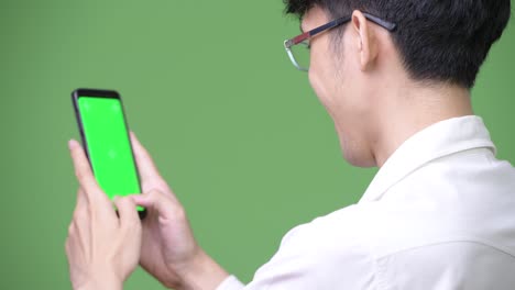 Young-Asian-businessman-using-phone-while-showing-copy-space